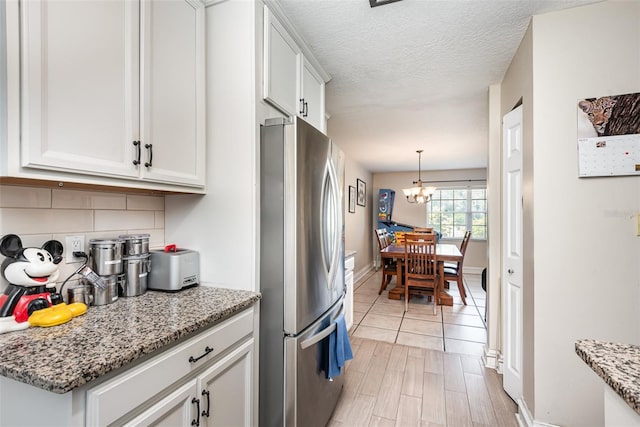 kitchen with decorative backsplash, light stone countertops, white cabinets, a chandelier, and stainless steel refrigerator