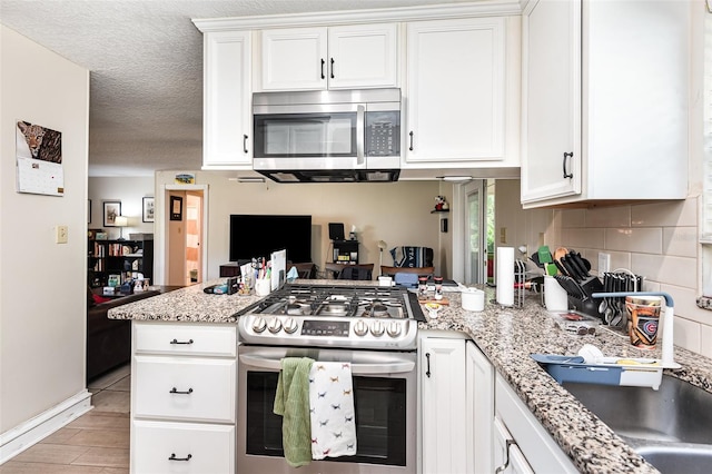 kitchen featuring kitchen peninsula, white cabinetry, light stone counters, and appliances with stainless steel finishes