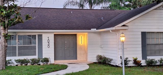 doorway to property featuring roof with shingles and a yard