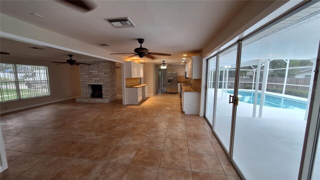 unfurnished living room with light tile patterned floors, a fireplace, ceiling fan, and plenty of natural light