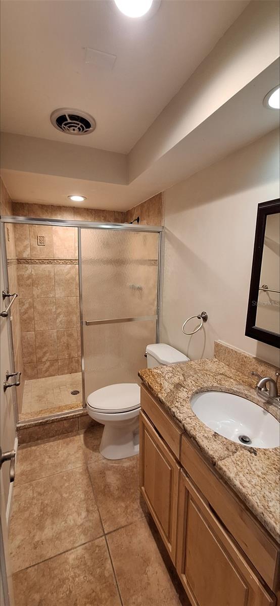 bathroom with tile patterned flooring, a shower with door, toilet, and vanity