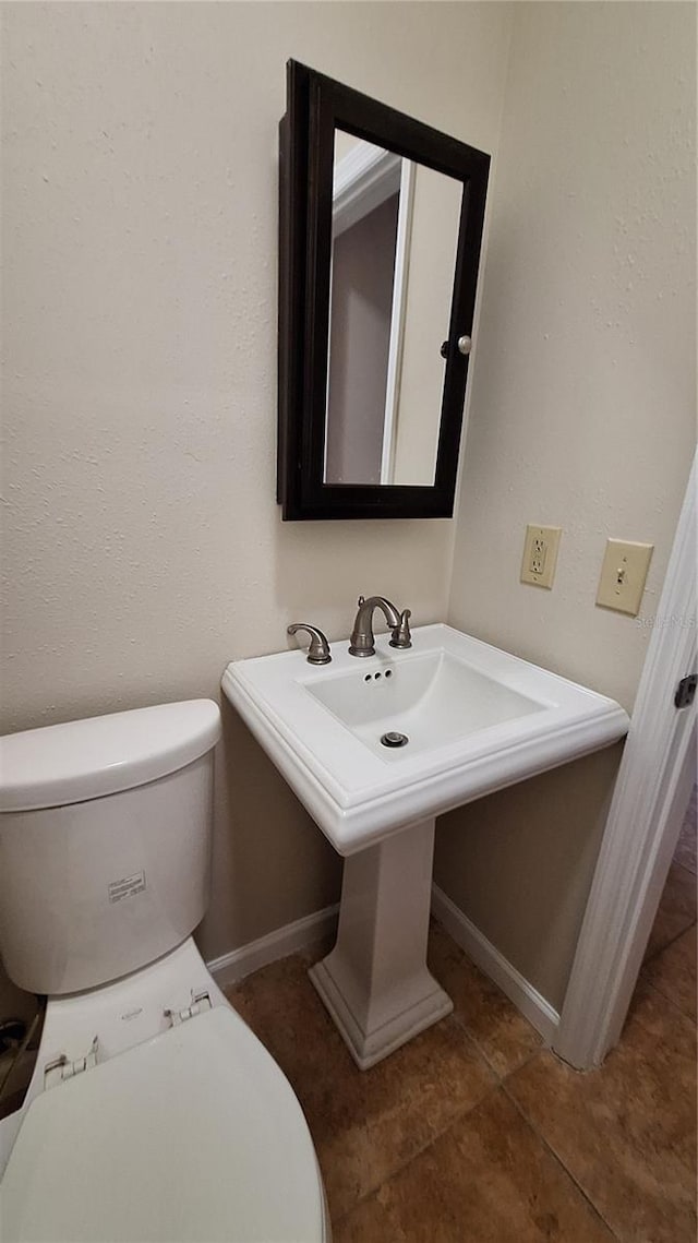 half bath featuring tile patterned floors, a sink, toilet, and baseboards