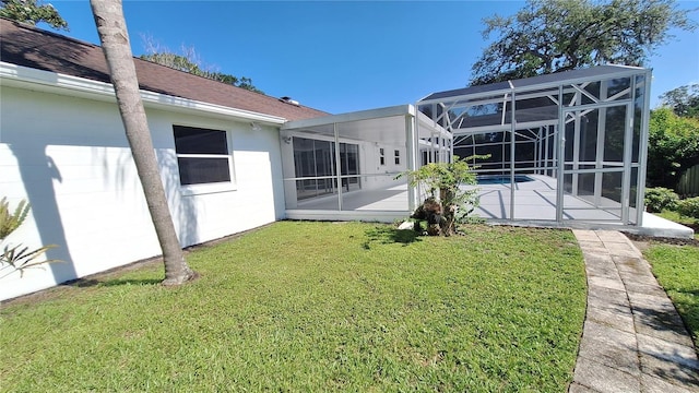 rear view of property featuring a yard, a patio, and glass enclosure