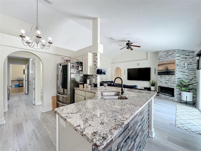 kitchen featuring stainless steel fridge, light stone countertops, sink, and vaulted ceiling