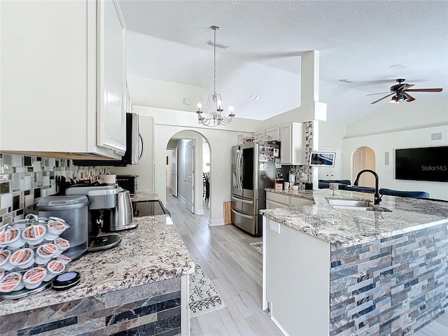 kitchen with sink, light stone counters, stainless steel refrigerator with ice dispenser, kitchen peninsula, and lofted ceiling