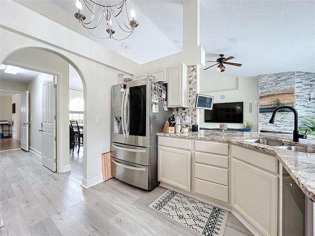 kitchen with sink, light stone counters, stainless steel refrigerator with ice dispenser, lofted ceiling, and ceiling fan with notable chandelier