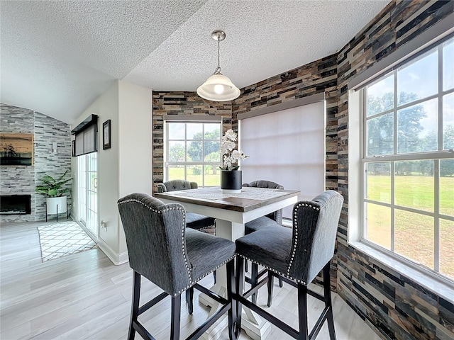 dining area with hardwood / wood-style flooring, lofted ceiling, a textured ceiling, and a tiled fireplace