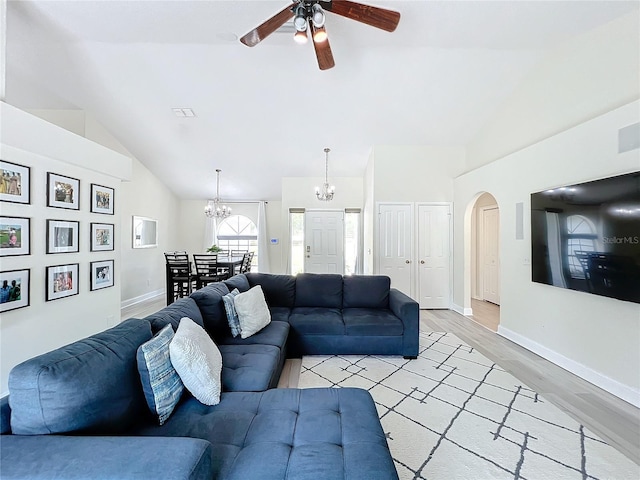 living room featuring ceiling fan with notable chandelier, light hardwood / wood-style floors, and vaulted ceiling