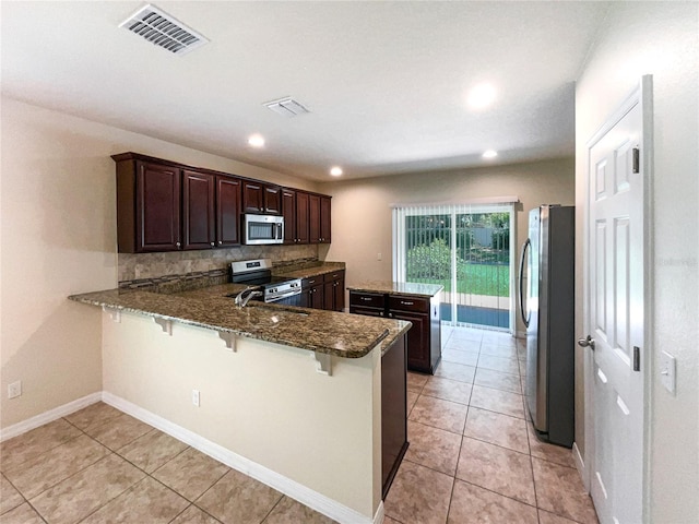 kitchen featuring a kitchen breakfast bar, decorative backsplash, kitchen peninsula, and stainless steel appliances