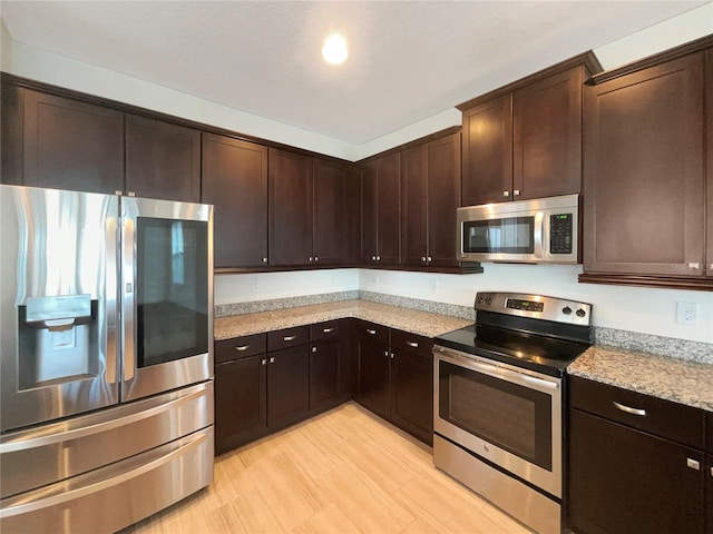 kitchen with appliances with stainless steel finishes, light stone countertops, dark brown cabinets, and light wood-type flooring