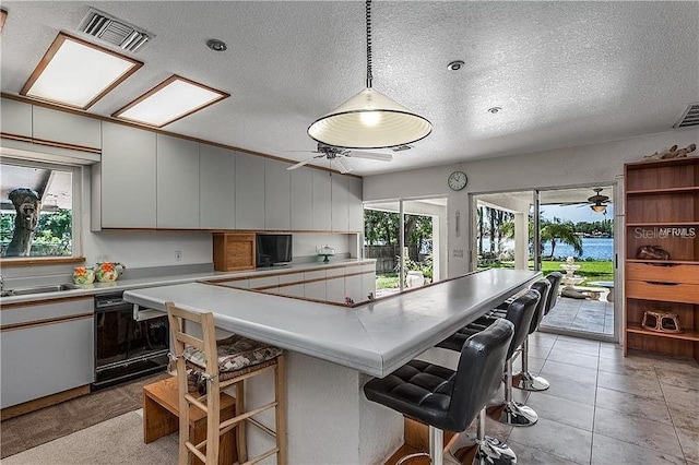 kitchen featuring ceiling fan, a breakfast bar area, visible vents, black dishwasher, and light countertops