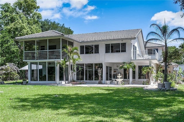 back of property featuring a ceiling fan, a yard, a balcony, and stucco siding