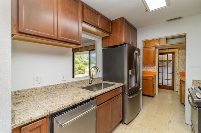 kitchen featuring tasteful backsplash, appliances with stainless steel finishes, light stone countertops, light tile patterned floors, and sink