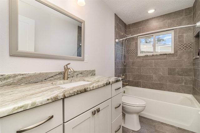 full bathroom featuring a textured ceiling, toilet, tile patterned floors, tiled shower / bath, and vanity