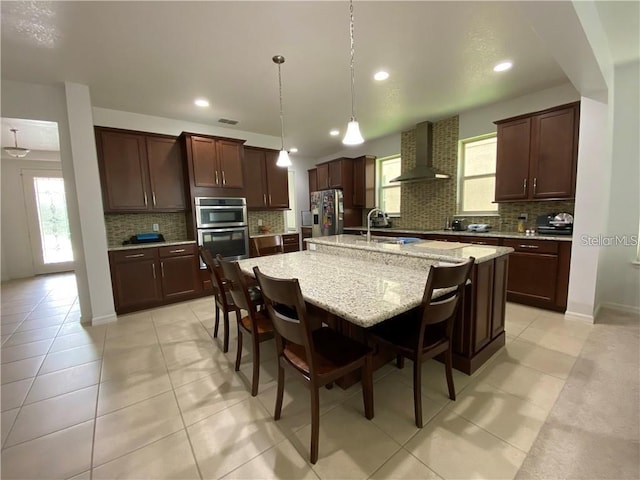 kitchen with tasteful backsplash, stainless steel appliances, wall chimney exhaust hood, a breakfast bar, and a kitchen island with sink