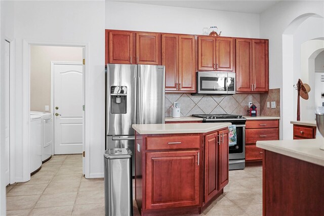 kitchen with tasteful backsplash, a kitchen island, light tile patterned floors, washing machine and clothes dryer, and stainless steel appliances