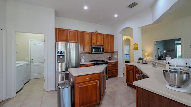 kitchen featuring light tile patterned floors, appliances with stainless steel finishes, sink, a center island, and washer and clothes dryer