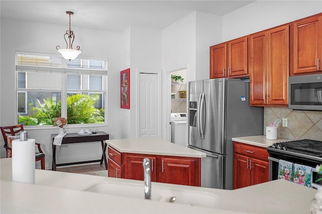 kitchen with a kitchen island, washer / dryer, pendant lighting, appliances with stainless steel finishes, and tasteful backsplash