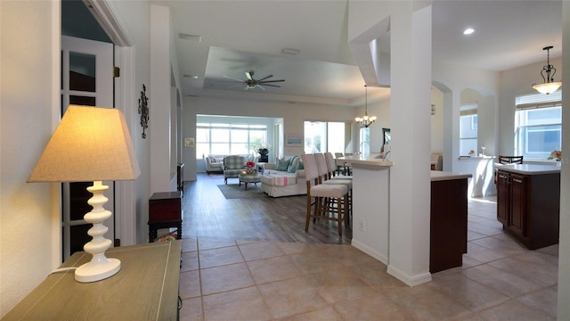 kitchen with a breakfast bar area, light wood-type flooring, ceiling fan with notable chandelier, pendant lighting, and dark brown cabinetry