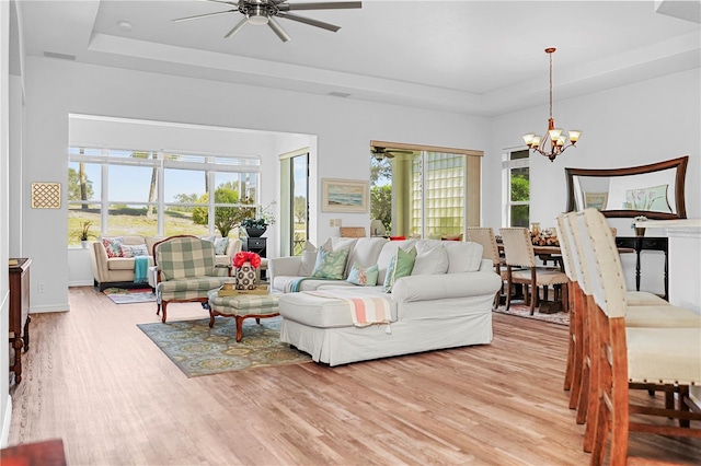 living room featuring light hardwood / wood-style floors, a tray ceiling, plenty of natural light, and ceiling fan with notable chandelier