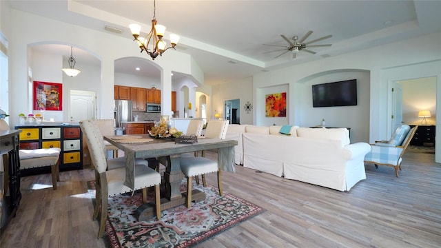 dining room featuring a tray ceiling, light wood-type flooring, and ceiling fan with notable chandelier