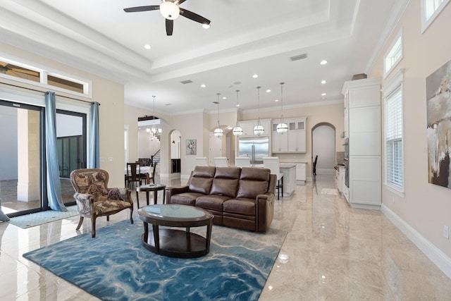 tiled living room featuring a tray ceiling, ornamental molding, ceiling fan with notable chandelier, and a wealth of natural light