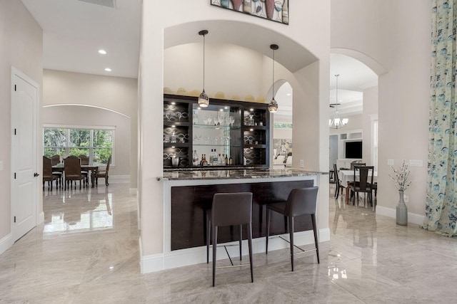 bar featuring a towering ceiling, dark stone countertops, light tile patterned floors, and an inviting chandelier