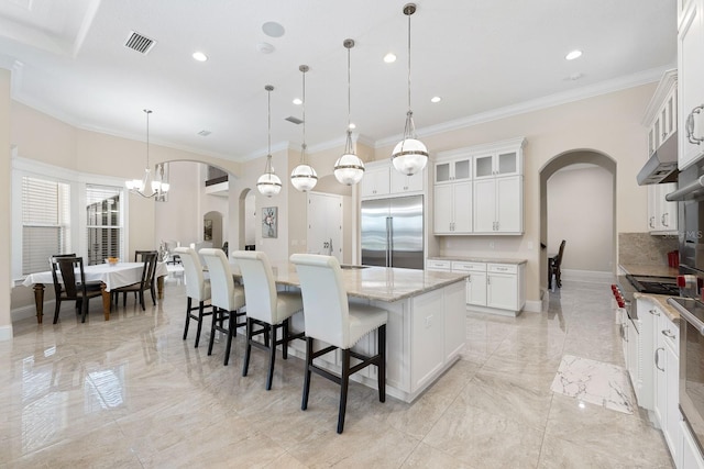 kitchen with decorative light fixtures, built in refrigerator, a center island, light stone counters, and light tile patterned floors