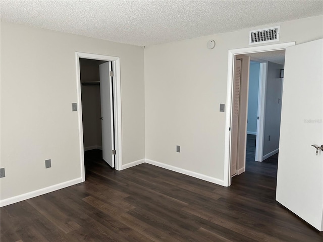 unfurnished bedroom with dark hardwood / wood-style flooring, a spacious closet, a textured ceiling, and a closet