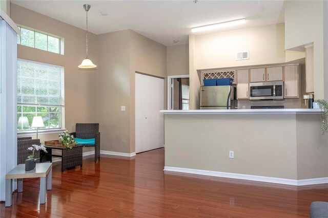 kitchen featuring hanging light fixtures, stainless steel appliances, kitchen peninsula, hardwood / wood-style floors, and a towering ceiling