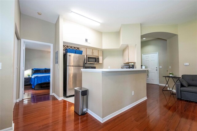 kitchen with a towering ceiling, kitchen peninsula, stainless steel appliances, a breakfast bar area, and hardwood / wood-style floors