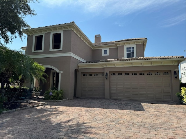 mediterranean / spanish house with a tile roof, a chimney, decorative driveway, and stucco siding