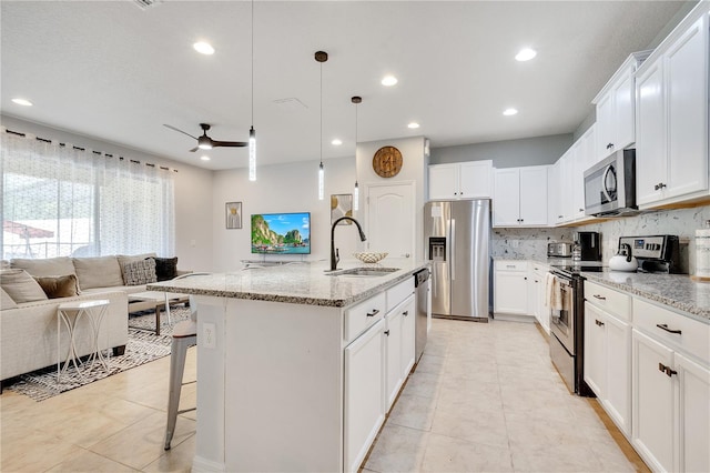 kitchen featuring light stone countertops, ceiling fan, stainless steel appliances, a center island with sink, and sink