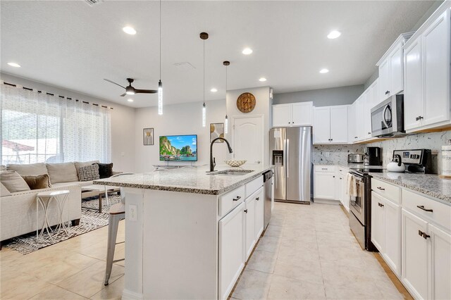 kitchen with stainless steel appliances, a sink, open floor plan, decorative backsplash, and light stone countertops