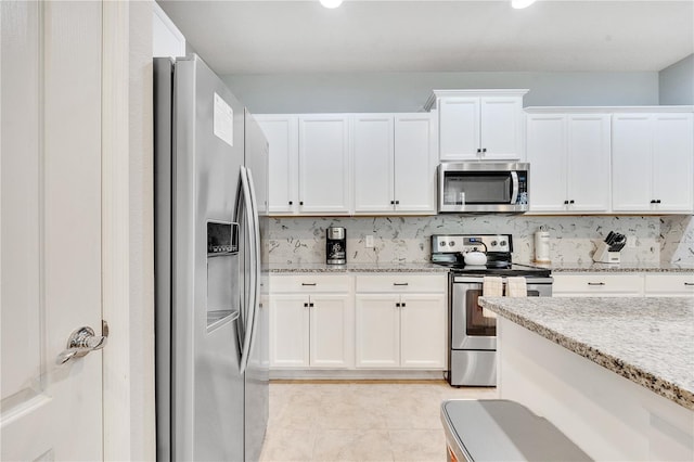 kitchen featuring light stone countertops, white cabinetry, appliances with stainless steel finishes, and backsplash