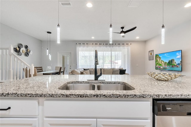 kitchen featuring visible vents, dishwasher, open floor plan, light stone countertops, and a sink