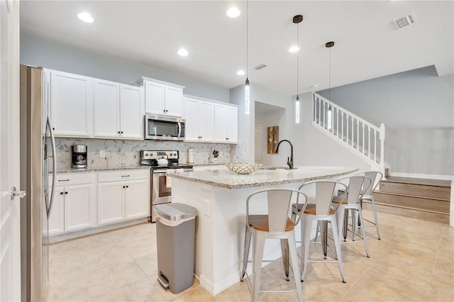 kitchen featuring a center island with sink, visible vents, appliances with stainless steel finishes, a sink, and light stone countertops