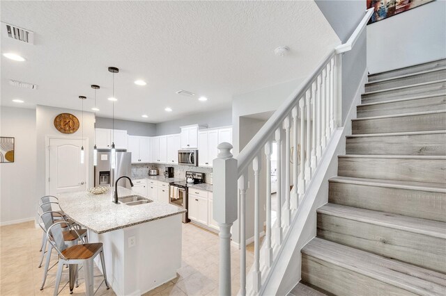 kitchen featuring light stone counters, tasteful backsplash, a kitchen island with sink, appliances with stainless steel finishes, and sink