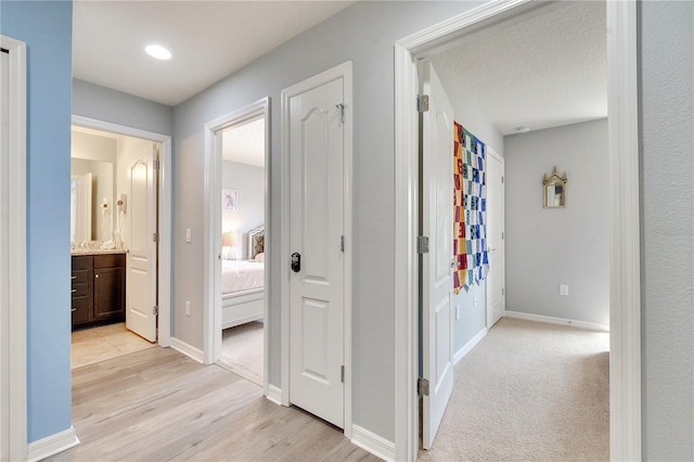 hall featuring light wood finished floors, baseboards, and a textured ceiling