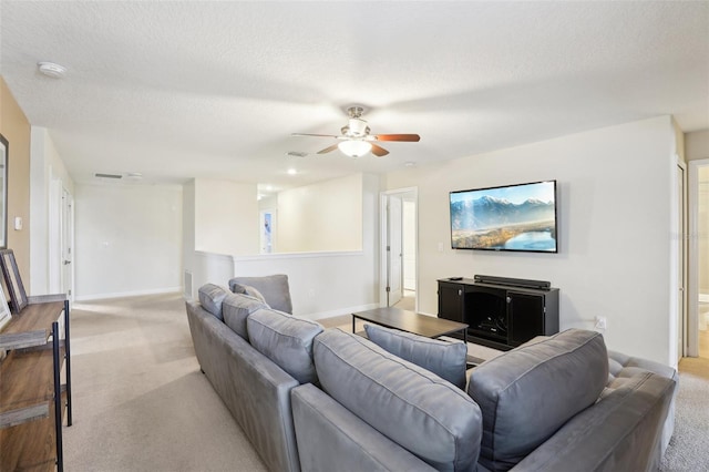 living room featuring ceiling fan, light colored carpet, and a textured ceiling