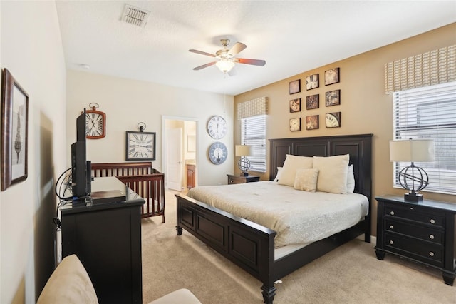 bedroom featuring ceiling fan, multiple windows, ensuite bathroom, and light carpet