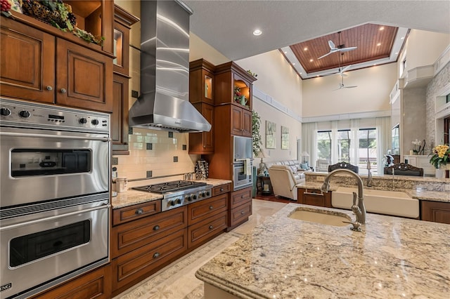 kitchen featuring light stone counters, stainless steel appliances, ceiling fan, wall chimney range hood, and high vaulted ceiling