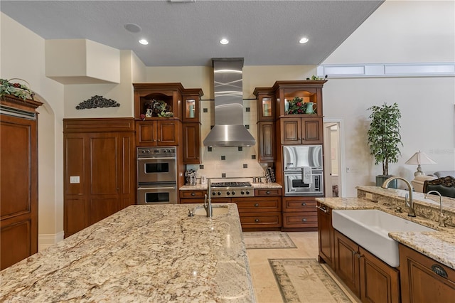 kitchen with light stone countertops, wall chimney range hood, sink, and appliances with stainless steel finishes