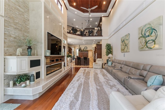 living room with a high ceiling, a raised ceiling, hardwood / wood-style flooring, ceiling fan, and a fireplace