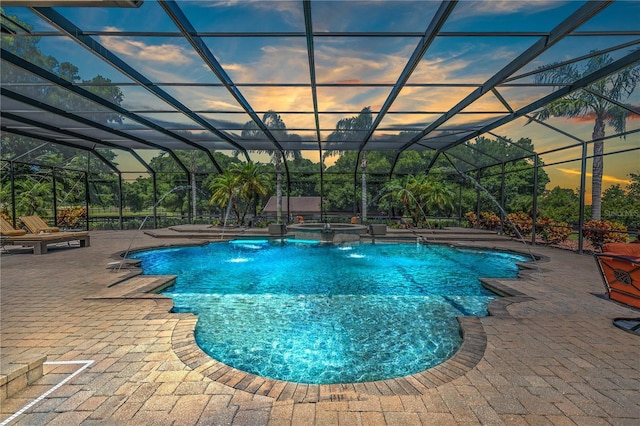 pool at dusk featuring pool water feature, glass enclosure, an in ground hot tub, and a patio