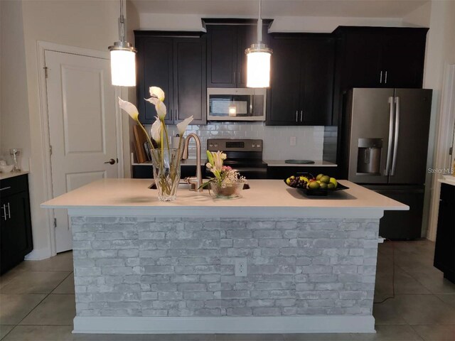 kitchen with hanging light fixtures, tasteful backsplash, a kitchen island with sink, light tile patterned floors, and appliances with stainless steel finishes