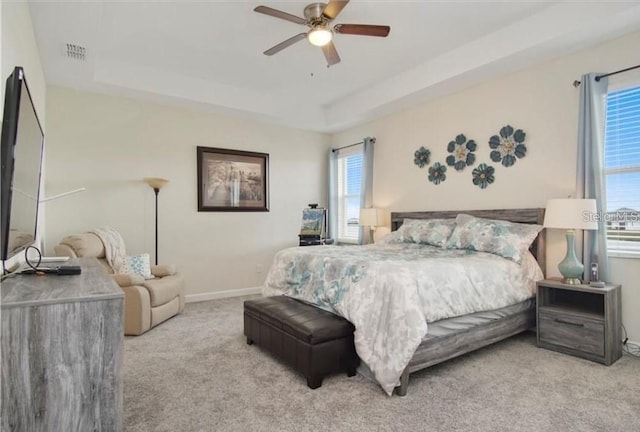 carpeted bedroom with a tray ceiling, multiple windows, and ceiling fan