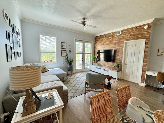 living room with a textured ceiling, ceiling fan, ornamental molding, and wooden walls