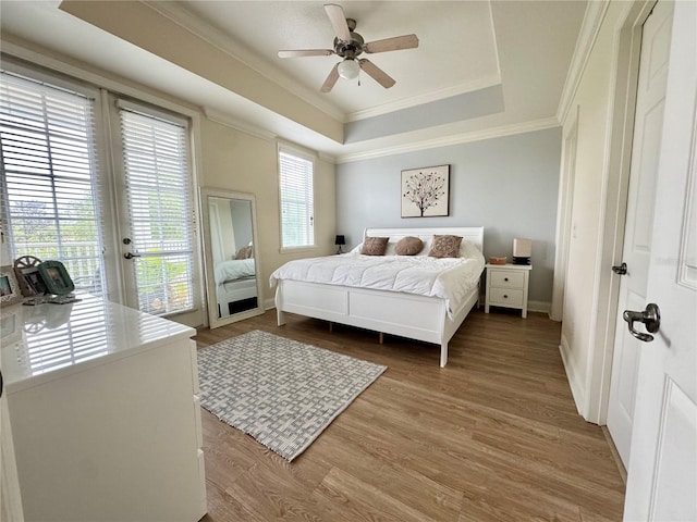 bedroom with hardwood / wood-style flooring, ceiling fan, a tray ceiling, access to exterior, and crown molding