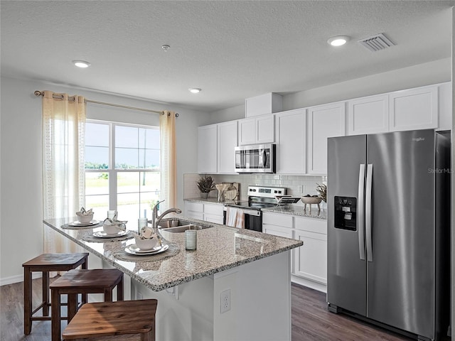 kitchen featuring a kitchen island with sink, white cabinets, light stone counters, dark hardwood / wood-style flooring, and stainless steel appliances